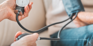 Profesional de la salud midiendo la presión arterial de una persona mayor con un tensiometro manual, en un entorno hogareño.
