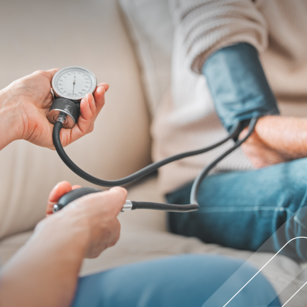 Profesional de la salud midiendo la presión arterial de una persona mayor con un tensiometro manual, en un entorno hogareño.