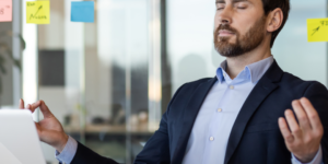 hombre con traje y barba realiza un ejercicio de respiración en su escritorio laboral