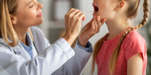 medica pediatra atiende a una niña y el revisa la garganta en su consultorio
