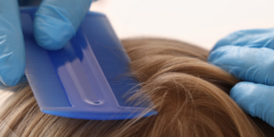 unas manos con guantes azules pasan un peine para la pediculosis por el cabello de un niño