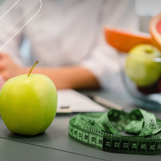 escritorio de un médico nutricionista en el que se ven unas frutas y cinta para medir